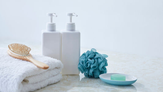 Banyo tezgâhında pompalı beyaz bakım şişeleri, havlu, saç fırçası ve duş lifi